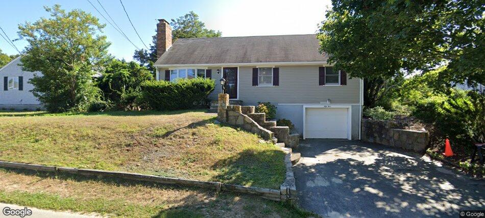Beige ranch-style house with a brick chimney, stone staircase to the front door, and a tucked-under garage beneath the home.